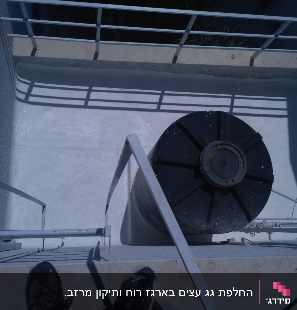 מיכל מים שחור על גג עם מעקה מתכת